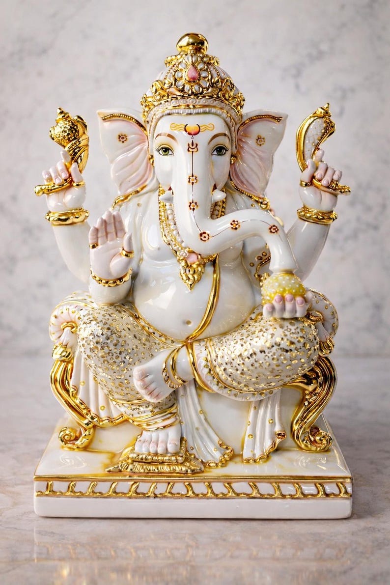 May include: A white ceramic statue of Ganesha seated on a base, featuring gold-painted accents on the crown, jewelry, and clothing. The figure has four arms, holding a conch shell and a lotus, with one hand raised in a gesture of blessing.
