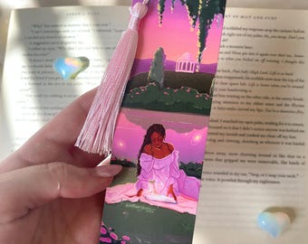 Peut inclure: Un marque-page rectangulaire en papier illustré d'une personne en robe blanche assise sur l'herbe au coucher du soleil, avec un bâtiment à dôme en arrière-plan. Le marque-page possède un pompon en soie rose clair attaché au trou supérieur.