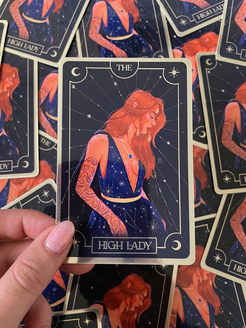 May include: A tarot card with a gold border and a dark blue background. The card depicts a woman with red hair wearing a blue dress with stars and constellations. The card is titled "The High Lady".