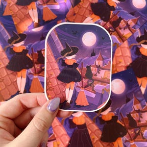 May include: A die-cut sticker featuring an illustration of a figure in a black dress and pointed hat standing on a tiled roof at night. A black cat sits nearby, a broom rests against the roof, and a full moon shines in the purple sky above.