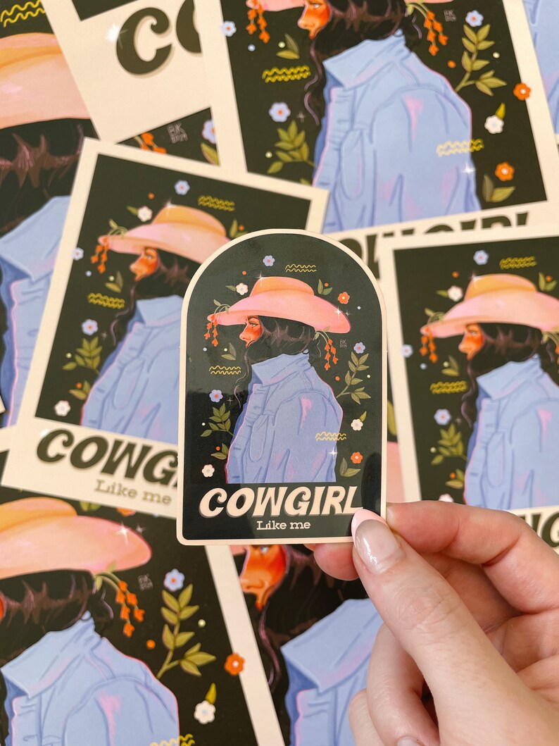 May include: A sticker with a black background and a woman wearing a pink cowboy hat and a blue denim jacket. The sticker has the text "COWGIRL Like me" in white letters.