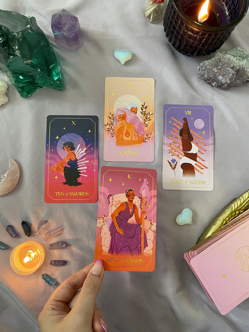 May include: Four tarot cards laid out on a purple surface with crystals and a lit candle. The cards are "Ten of Swords", "Lovers", "Eight of Wands", and "King of Wands".