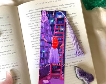 May include: A fantasy bookmark depicting a person with red hair on a ladder, reaching for books in a library setting. The bookmark has a purple tassel and is placed on an open book. The illustration includes a starry night sky.