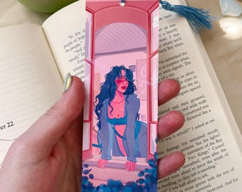 Peut inclure: Un marque-page rose et bleu avec une femme en robe bleue regardant par une fenêtre. L'arrière-plan est un motif floral bleu et violet. Le marque-page porte le texte "Ok, Bay".