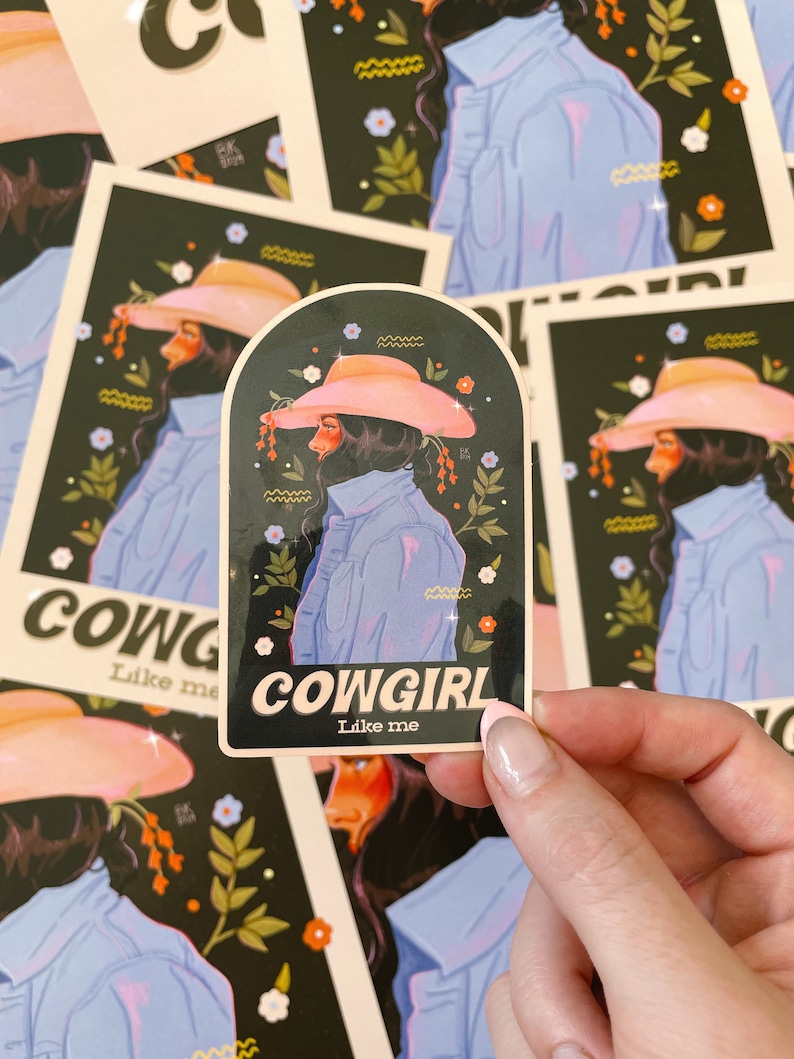 May include: Cowgirl sticker with a black background, pink flowers, and a woman wearing a pink cowboy hat and a blue denim jacket. The sticker says "COWGIRL Like me".