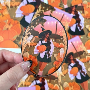Puede incluir: Una pegatina ovalada con la ilustración de una persona con sombrero de bruja, camisa blanca y falda oscura, sosteniendo una calabaza naranja en un campo con tallos de maíz, pequeños fantasmas y luces de cadena bajo un cielo atardecer.