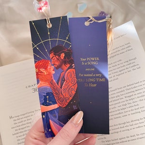 May include: Two bookmarks featuring a couple with a starry night sky background. The bookmark on the left has a quote that reads "Your power is a song and one." The bookmark on the right has a quote that reads "I've waited a very long time to hear."