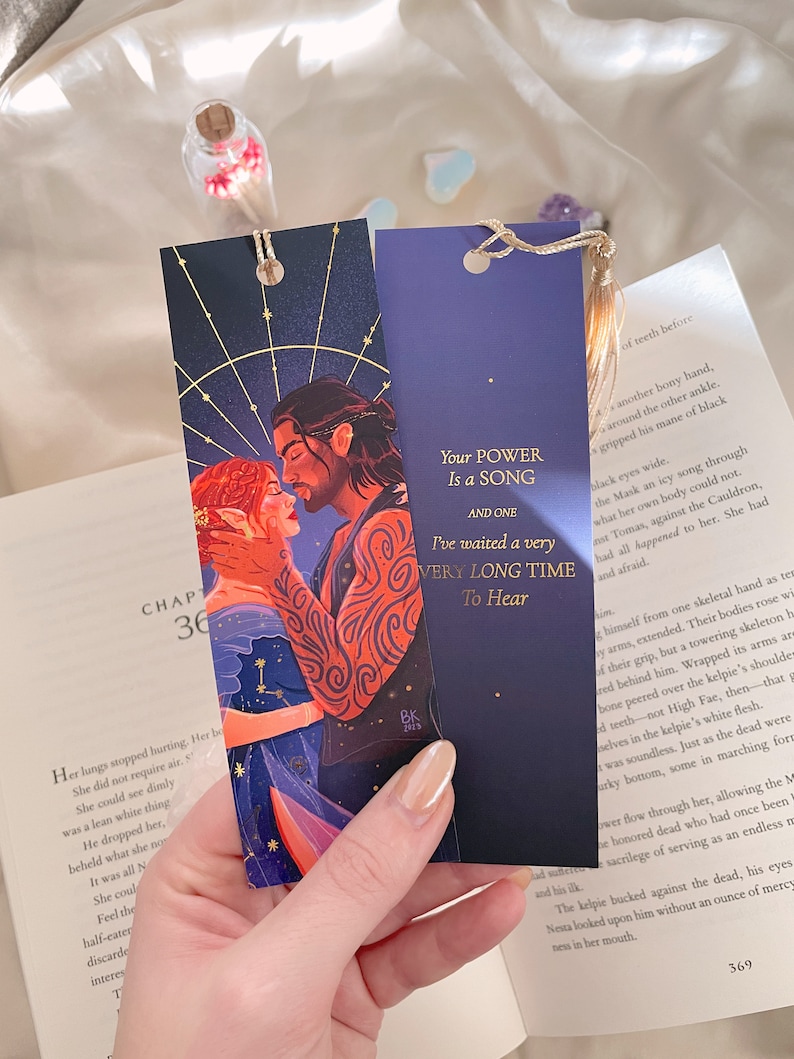 May include: Two bookmarks featuring a couple with a starry night sky background. The bookmark on the left has a quote that reads "Your power is a song and one." The bookmark on the right has a quote that reads "I've waited a very long time to hear."