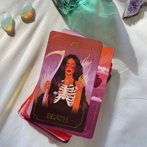 May include: A tarot card with a woman with long black hair and a skeletal ribcage. The card is red, purple, and gold with the word "DEATH" printed on it.