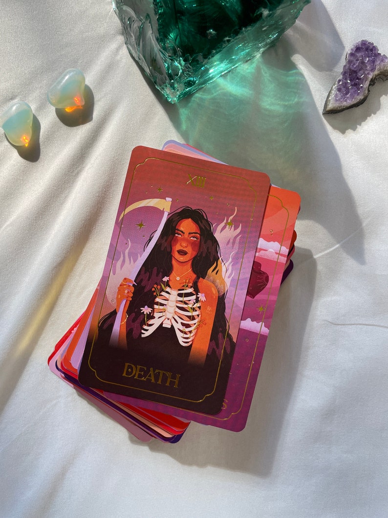 May include: A tarot card with a woman with long black hair and a skeletal ribcage. The card is red, purple, and gold with the word "DEATH" printed on it.
