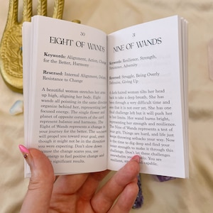 May include: Two open pages from a book about tarot cards. The pages are open to the Eight of Wands and the Nine of Wands cards. The cards are illustrated with women and wands. The text on the pages describes the meaning of the cards.