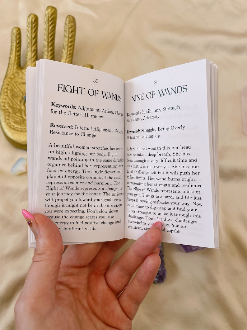 May include: Two open pages from a book about tarot cards. The pages are open to the Eight of Wands and the Nine of Wands cards. The cards are illustrated with women and wands. The text on the pages describes the meaning of the cards.