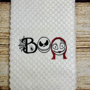 May include: White kitchen towel with an embroidered "BOO" design featuring the characters Jack Skellington and Sally from the movie The Nightmare Before Christmas.