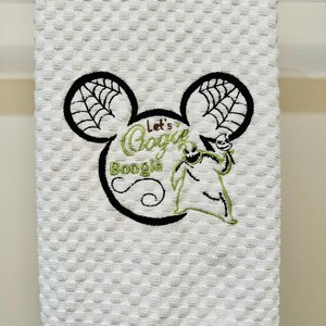 May include: White kitchen towel with an embroidered Mickey Mouse head design. The ears have a spiderweb pattern. The text "Let's Boogie" is inside the head with a green Oogie Boogie character.