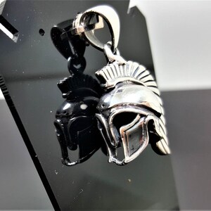 May include: Silver pendant in the shape of a Roman helmet with a plume on top. The pendant is on a black display stand.