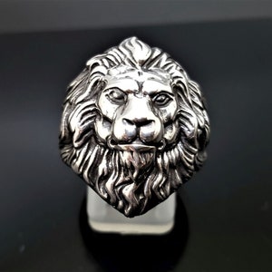 May include: A silver ring with a detailed lion head design. The lion's mane is intricately sculpted and the face is realistic.