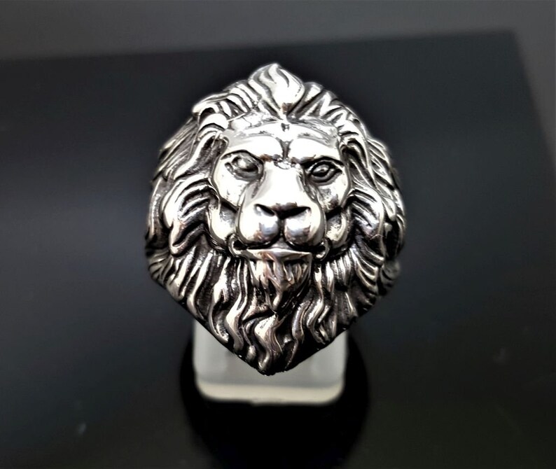May include: A silver ring with a detailed lion head design. The lion's mane is intricately sculpted and the face is realistic.