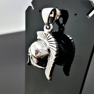 May include: Silver pendant in the shape of a Roman soldier's helmet with a detailed design.