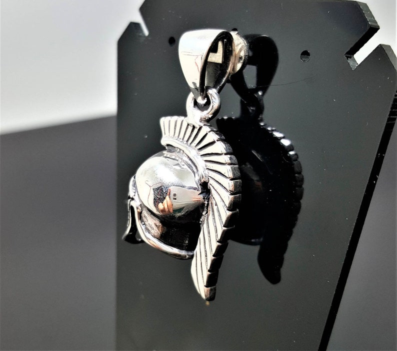 May include: Silver pendant in the shape of a Roman soldier's helmet with a detailed design.