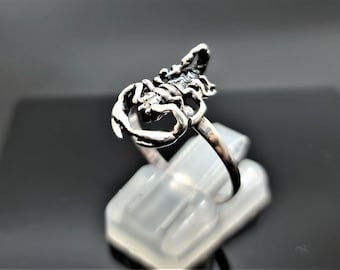 May include: A silver ring with a scorpion design. The scorpion is detailed and has a raised tail.