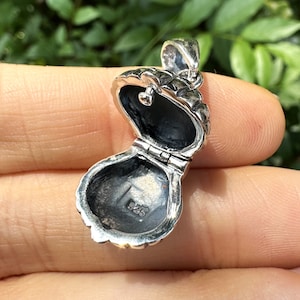 Peut inclure: Pendentif en argent en forme de locket avec un design de coquille détaillé. Le locket est ouvert, révélant un intérieur vide. Le locket est marqué "925" à l'intérieur.