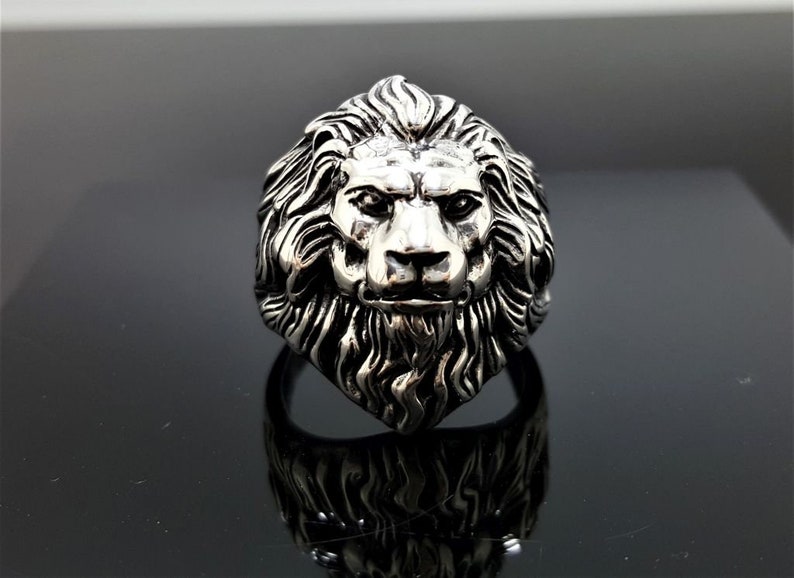 May include: A silver ring with a detailed lion head design. The lion's mane is intricately sculpted and the ring has a polished finish.