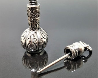 May include: A silver bottle stopper with an intricate floral design. The stopper is attached to a long, thin silver rod.