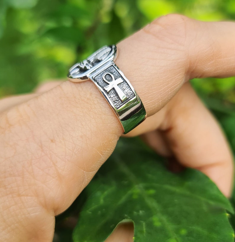 May include: A silver ring with an ankh symbol and a textured design. The ring is worn on a finger.