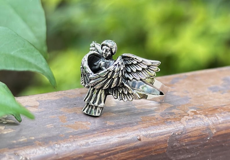 May include: A silver ring featuring a detailed sculpture of an angel with outstretched wings.