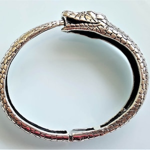 May include: A silver snake bangle bracelet with a detailed snake head design. The bracelet is open and has a hinged clasp.
