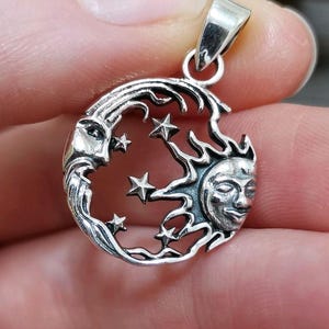 Peut inclure: Pendentif en argent représentant une lune croissante avec un visage, un soleil avec un visage et des étoiles. Le pendentif est conçu dans un style détaillé et complexe.