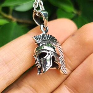 May include: Silver pendant necklace featuring a detailed depiction of a Spartan helmet. The helmet is a classic symbol of strength and courage.