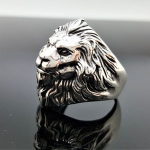 May include: A silver ring with a detailed lion head design. The lion's head is facing to the side and has a textured mane.