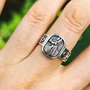 May include: Silver ring with an Anubis head design. The ring has a rectangular shape and is engraved with the Anubis head in the center. The ring is worn on a finger.