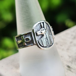 May include: Silver ring with an ankh symbol and an image of an Egyptian god's head.