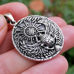 May include: Silver pendant featuring a detailed design of a scarab beetle with wings spread, a sunburst, and a geometric flower of life symbol.