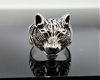 May include: A silver ring featuring a detailed wolf's head design. The wolf's head is facing forward with its mouth closed. The ring is made of sterling silver and has a polished finish.