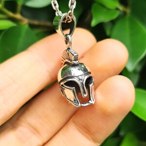 May include: Silver pendant necklace featuring a detailed Spartan helmet design. The helmet is a symbol of strength and courage.