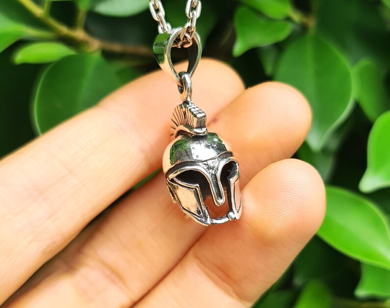 May include: Silver pendant necklace featuring a detailed Spartan helmet design. The helmet is a symbol of strength and courage.