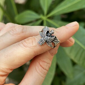 May include: Silver ring featuring a detailed angel design with outstretched wings.