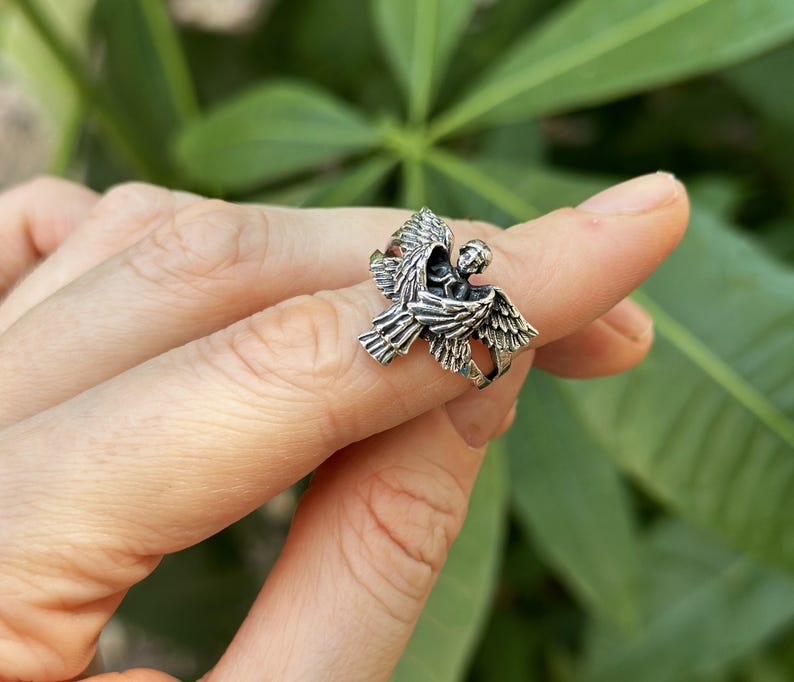 May include: Silver ring featuring a detailed angel design with outstretched wings.
