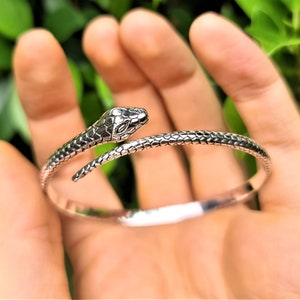 May include: Silver snake bracelet with a detailed snake head design. The bracelet is open and adjustable.