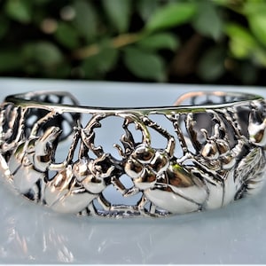 Pode incluir: Pulseira de prata com um design detalhado de besouros e folhas. A pulseira é aberta e ajustável.