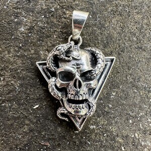 May include: Silver pendant featuring a skull with a snake wrapped around it, set within a triangle.