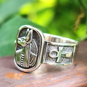 May include: Silver ring with an ankh symbol and an image of the Egyptian god Anubis on the front.