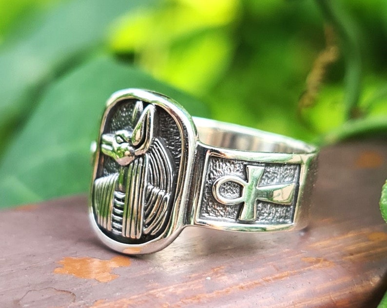May include: Silver ring with an ankh symbol and an image of the Egyptian god Anubis on the front.