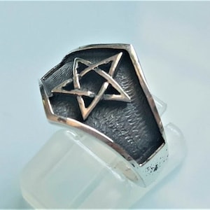 May include: A silver ring featuring a five-pointed star design. The star is raised and has a textured surface.