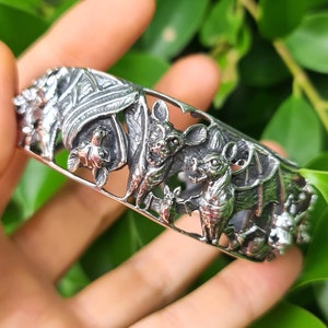 Può includere: Braccialetto d'argento con un designo dettagliato di pipistrelli e foglie. Il braccialetto è aperto e ha un design delicato e intricato.