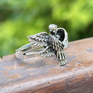 May include: A silver ring with an angel design. The angel is depicted with wings outstretched and a halo. The ring is made of sterling silver and is a great gift for anyone who loves angels.