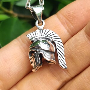 May include: Silver pendant necklace featuring a detailed Spartan helmet design. The helmet has a crested plume and a face mask.